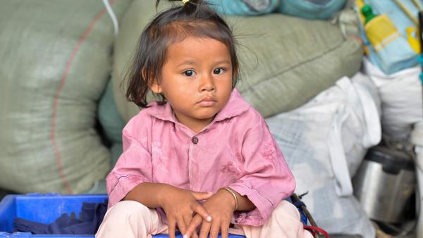 Une petite fille assise devant des sacs de riz distribués par PSE