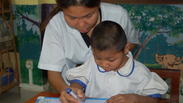 Une éducatrice spécialisée aide un enfant porteur de handicap à écrire