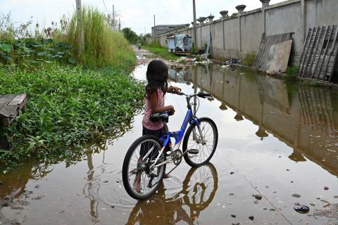 Une petite fille à côté de son vélo devant une ruelle inondée Une petite fille à côté de son vélo devant une ruelle inondée