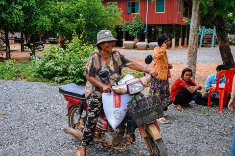 Une maman avec son sac de riz sur sa moto après une distribution de riz à Oudong Une maman avec son sac de riz sur sa moto après une distribution de riz à Oudong