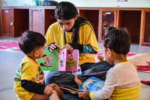 Les bébés regardent un livre d'images avec une monitrice des camps Les bébés regardent un livre d'images avec une monitrice des camps